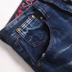 Detailopname van blauwe herenjeans met contrasterende rode stiksels en metalen klinknagels.