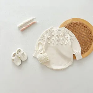 Detailed view of cream baby knit romper with hollow-out pattern and cute pom-poms for autumn.
