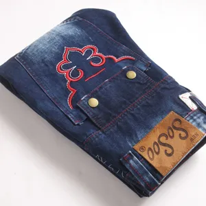Gedetailleerd overzicht van donkerblauwe stretch denim broek met rode borduursel en leer.