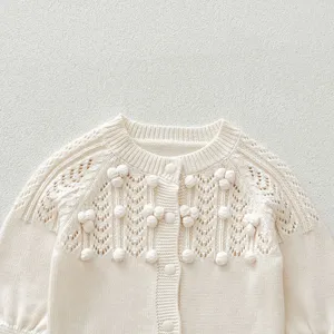 Detailed view of baby girl knit cardigan, hollowed out pattern and cute pom poms, round neck.