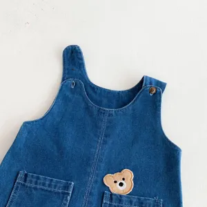Close up view of cute kids denim overalls featuring a lovely bear patch and front pockets.