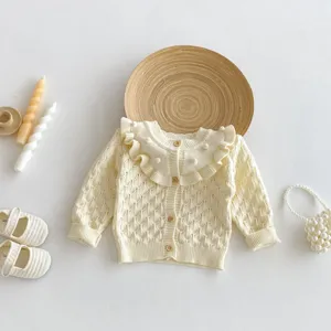 Cute baby knitted cardigan featuring a sweet ruffled collar and wooden buttons. Cozy toddler top.
