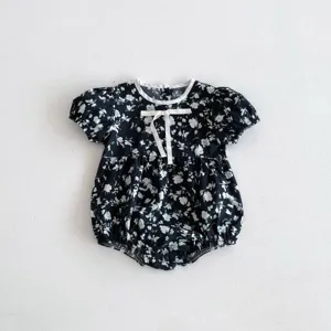 Detailansicht des süßen Baby Stramplers mit Blumenmuster, kurzen Ärmeln und weißer Schleife.