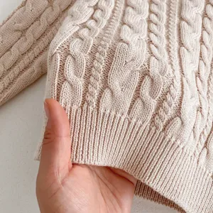 Close-up of baby cable knit sweater fabric showing soft texture and classic woven pattern details.