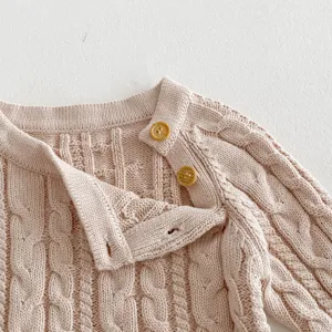 Detail shot of baby knit sweater collar and shoulder buttons, soft pink cable knit texture.