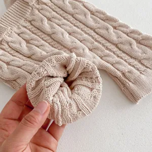 Infant cable knit baby jumpsuit detail, soft beige cotton material, cozy autumn outfit.