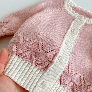 Cute baby pink knit cardigan sweater detail showing delicate hollow-out pattern and buttons.