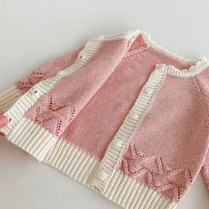 Close up detail of baby girl pink knit cardigan sweater showing hollow-out pattern and buttons.