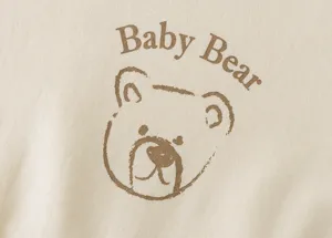 Close-up detail of soft beige cotton fabric featuring a cute bear print and Baby Bear text.