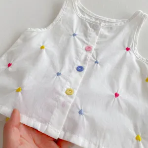 Vista dettagliata del top bianco in cotone per bambina con ricami di cuori colorati e bottoni.