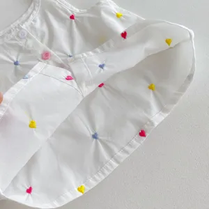 Dettaglio del top in cotone bianco per bambina con ricamo colorato e bottoni.