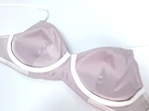 Vista detallada del sujetador de satén rosa sin aros con ribete blanco, textura de tela de cerca