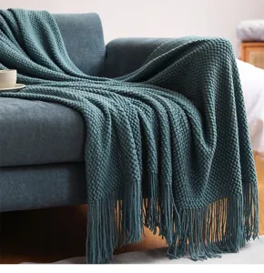 Knitted blanket detail showing pineapple grid texture and soft fringe drape on a cozy sofa.