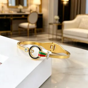 Gold titanium steel hinge bangle with crystal, black enamel and red green stripe detail.