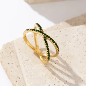 Primer plano detallado de un anillo cruzado bañado en oro con circonitas verdes.