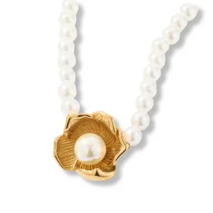 Detalle de collar de perlas con colgante de flor dorada y perla central brillante.