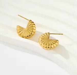 Primer plano de pendientes de aro texturizados chapados en oro de 18k sobre fondo de ondas blancas.