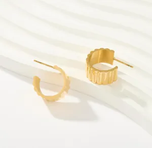 Primer plano de pendientes de aro en C de acero de titanio bañado en oro de 18k con borde ondulado.