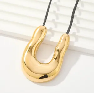 Primer plano detallado de un collar con dije dorado en forma de U, diseño moderno minimalista.