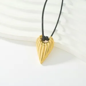 Detalle de collar con colgante de lágrima acanalado bañado en oro sobre fondo blanco ondulado.