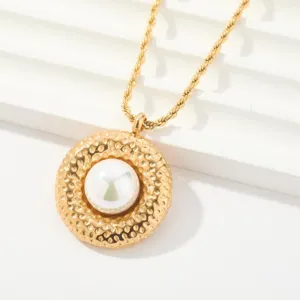 Primer plano detallado de un collar con colgante texturizado dorado con perla blanca.