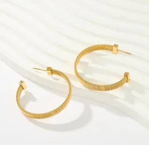 Close-up detail of trendy gold coiled hoop earrings featuring unique spring texture and square ends.