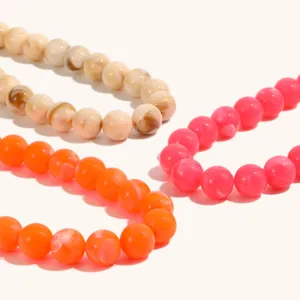 Primo piano dettagliato di collane di perle colorate, con opzioni arancioni, rosa e effetto marmo.