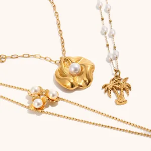 Detailed closeup of 18k gold plated stainless steel pearl flower and palm tree necklace set.