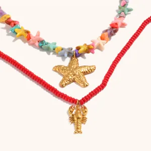 Primo piano di collana a doppio strato con perle di stelle marine e ciondolo aragosta dorato.