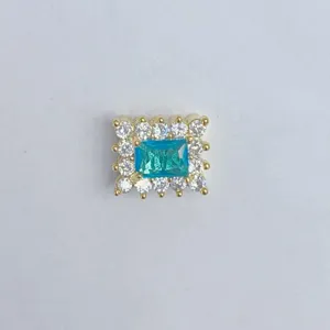 Primo piano del ciondolo in rame dorato con uno zircone blu vivido e pietre di contorno chiare.