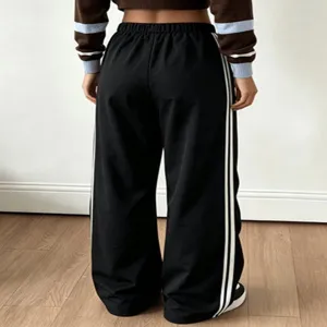 Dettaglio posteriore di pantaloni sportivi neri larghi con eleganti strisce laterali bianche.