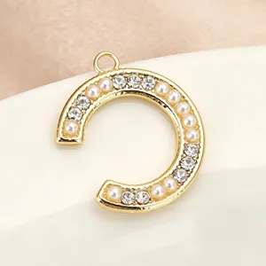 Close-up detail of a gold letter C DIY jewelry pendant embedded with pearls and rhinestones.