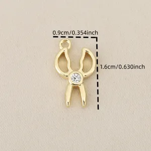 Dettaglio del ciondolo a forbice dorata con dimensioni di 1,6 cm e zircone brillante.