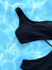 Detailed shot of a sleek black one-shoulder swimsuit, highlighting premium fabric and cut.
