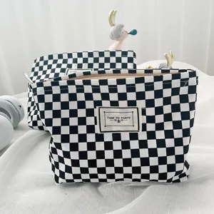 Black and white checkered canvas cosmetic pouch detail view with zipper and woven label.