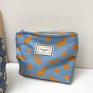 Blue fabric cosmetic bag with orange floral pattern and zip closure for daily travel use.