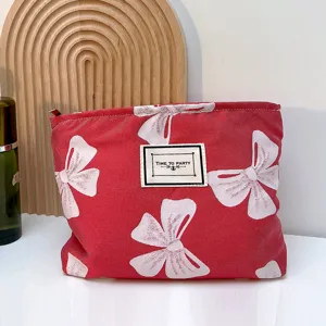 Nahaufnahme der roten Kosmetiktasche mit weißem Schleifenmuster und gewebtem Etikett vorne.