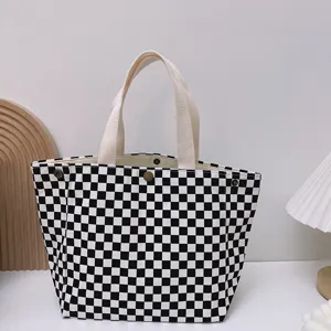 Detalle del bolso tote de lona a cuadros blancos y negros, con asas resistentes y botón de presión.