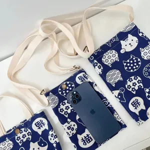 Vista detallada del bolso cruzado de lona azul y blanca con diseño de gato y correa ajustable.