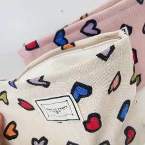 Dettaglio borsa cosmetica in velluto a coste con motivo a cuori colorati e cerniera.