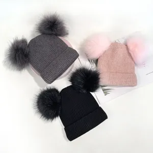 Close-up detail of three fluffy double pom pom knit beanie hats in grey, pink, and black colors.