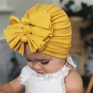 Closeup of adorable baby wearing soft yellow knotted bow turban hat, cute infant headwear.