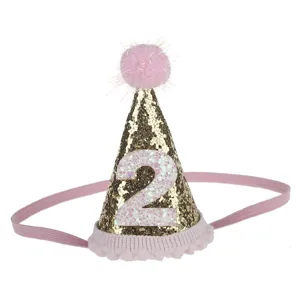 Primo piano dettagliato di un cappello da compleanno dorato con pon-pon rosa brillanti.
