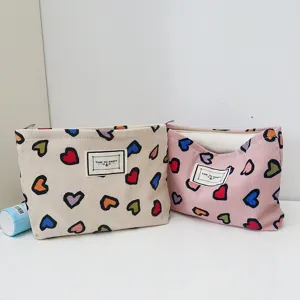 Dettaglio della borsa cosmetica in tela con stampa a cuori colorati, zip e etichetta.