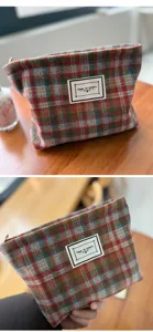 Detail shot of tweed plaid cosmetic pouch, showing textured woolen fabric and custom label.