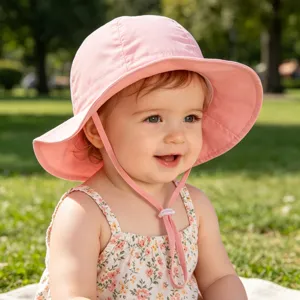 Close-up detail of cute baby wearing pink outdoor sun protection bucket hat in park.