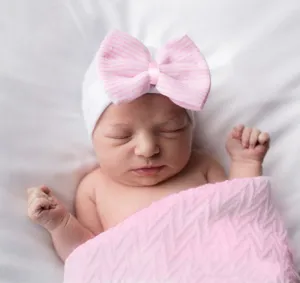 Gorro blanco para recién nacido con gran detalle de lazo rayado rosa, primer plano suave y cómodo.
