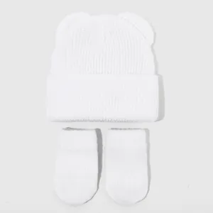Detailansicht von weißem Babymütze mit Bärenohren und passenden Handschuhen, weicher Strickstoff.