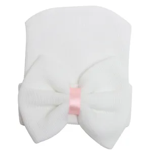 Adorable gorro de punto blanco para recién nacido con gran lazo y cinta rosa bonita.