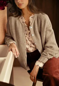 Casual knitted cardigan detail featuring crew neck and button closure in a cozy room.